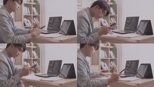 一位亚洲设计师用他的智能手机交流。完成项目和论文。在家里用笔记本电脑在桌子上工作。高清在线视频素材下载