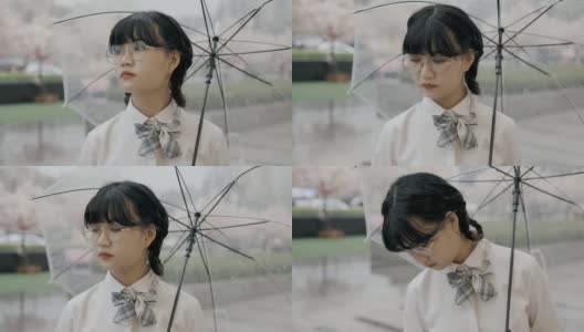 可爱的亚洲女生，穿着校服，打着伞，站在街上高清在线视频素材下载