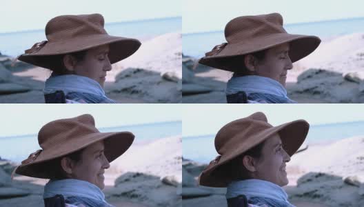 一个快乐的年轻女孩戴着帽子微笑着站在海滩上高清在线视频素材下载
