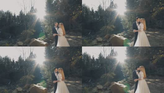 一对年轻美丽的新婚夫妇站在瀑布附近的森林里接吻。阳光灿烂的婚礼。慢动作高清在线视频素材下载