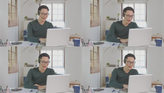微笑英俊的亚洲商人戴着耳机在家远程工作。他是一个网络视频会议高清在线视频素材下载