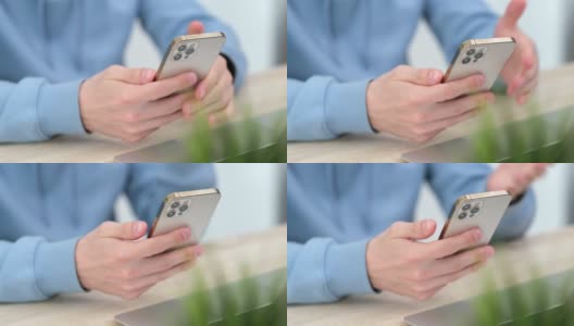 4 k。男子使用iPhone 12智能手机按手指，阅读社交媒体，打字或在线购物。在家里或工作时用双手拿手机。在俄罗斯圣彼得堡24.04.21号桌高清在线视频素材下载