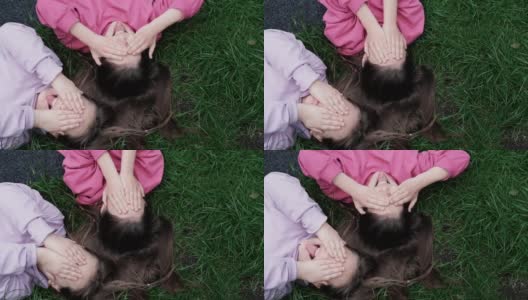 两个漂亮的千禧一代朋友躺在公园或草坪上的绿草地上。白人女孩笑着一起玩。俯视图的镜头高清在线视频素材下载