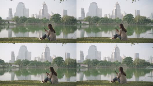 亚洲妇女是快乐的放松，在一个城市公园的电话聊天在早上，人们放松在城市的自然环境高清在线视频素材下载