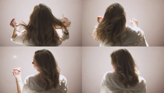 一个年轻的女人在米色的墙壁背景上摇着她金色的卷发。艺术。后视图，一个年轻的金发女人在一个白色的衬衫摆姿势和触摸她的头发。高清在线视频素材下载