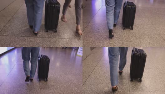 女人穿着牛仔裤长裤，黑色鞋跟鞋，带着黑色行李箱沿着机场航站楼走着，看腿的底部。高清在线视频素材下载