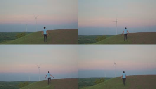 日落时分，印度古吉拉特邦万卡纳，一名印度男子在风电场的风车前爬上小山。环境可持续性的背景。希望绿色能源取代化石燃料。高清在线视频素材下载