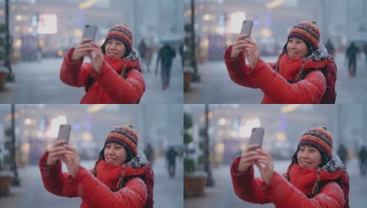 冬天，年轻的女游客在城市的雪地里用智能手机享受观光和自拍高清在线视频素材下载
