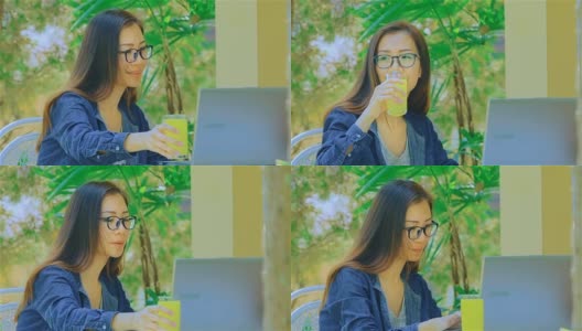 微笑的年轻女子打字在笔记本电脑和喝果汁在花园里高清在线视频素材下载