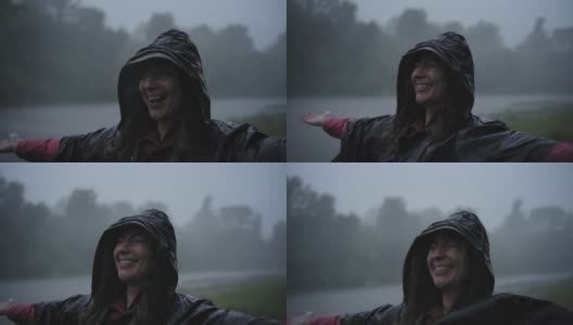 年轻的女孩穿着雨衣，在雨中微笑和大笑。从上面的肖像，女孩看着天空享受雨滴落在脸上，而站在大自然中。高清在线视频素材下载