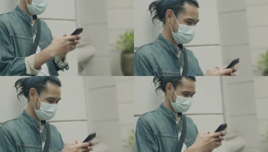 在covid-19大流行期间，一名年轻的亚洲男子戴着医用口罩，站在城市的街道上使用智能手机。高清在线视频素材下载
