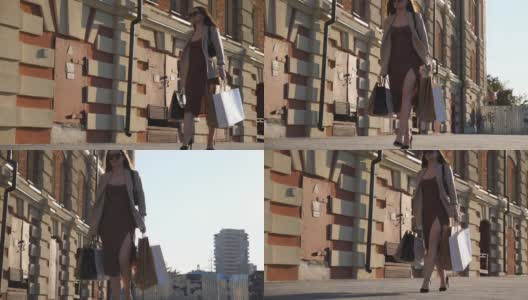 女顾客穿着漂亮的衣服，拿着购物袋在购物后走在人行道上。时尚苗条的女人拿着纸包走在城市的街道上。购物狂的概念。多莉拍摄慢动作高清在线视频素材下载