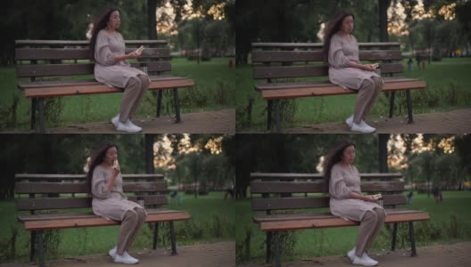宽镜头悲伤的老年孤独的女人吃三明治坐在公园的长椅上与自行车快速通过在前面。在春夏季的一天，绝望沮丧的白人退休老人独自在户外。高清在线视频素材下载