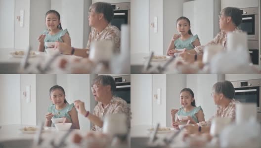 亚洲华裔孙女和她的祖母在厨房的柜台吃饺子高清在线视频素材下载