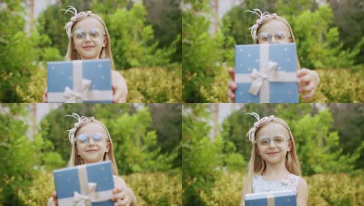 一个漂亮的7岁小女孩戴着眼镜，送了一个装在蓝色盒子里的带蝴蝶结的礼物。高清在线视频素材下载
