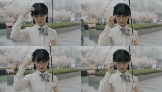 可爱的亚洲女生，穿着校服，打着伞，站在街上高清在线视频素材下载