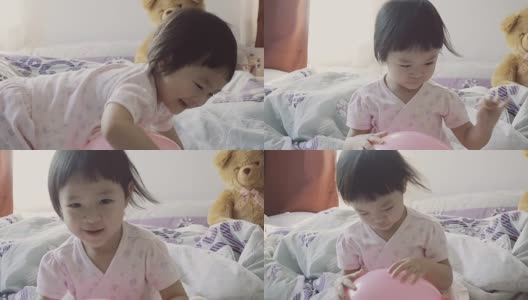 亚洲小女孩在床上玩粉红色的气球高清在线视频素材下载