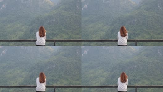模糊的后视图，一个女性旅行者坐在木制阳台上，看着美丽的山景高清在线视频素材下载
