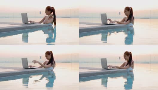 年轻的中国女子穿着白色比基尼在游泳池放松。女人享受工作，网上购物，检查社交网络，阅读新闻在舒适的笔记本电脑在早晨。高清在线视频素材下载