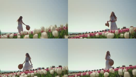 快乐的女孩在郁金香花园里转身。有创意的年轻女子欣赏鲜花高清在线视频素材下载
