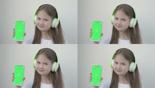 漂亮的白人女孩在大无线耳机显示手机与绿色屏幕模拟高清在线视频素材下载