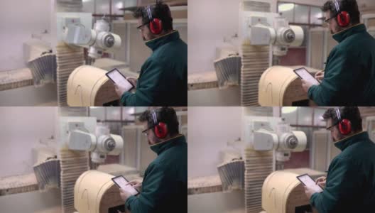 木匠戴着耳罩，通过数码板，在工厂调整和打开数控机床高清在线视频素材下载