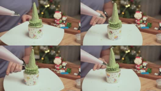 高视角:亚洲妇女的手从奶油榨汁机中榨取绿色奶油，在自制的圣诞树上做成树叶，作为庆祝圣诞节的甜点，12月假日在公寓里装饰圣诞树，礼盒，圣诞老人。高清在线视频素材下载