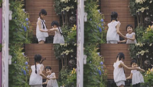 2个亚洲的中国年轻姐妹手牵着手，在周末的晚上在房子的前院跳来跳去，一起开怀大笑高清在线视频素材下载