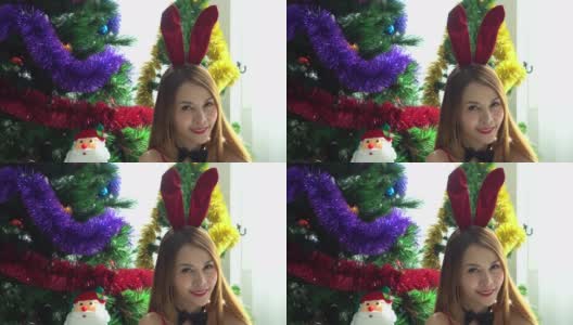 亚洲美丽的年轻女子在性感的红色内衣和兔子耳朵坐在白色的床上圣诞树的背景。性感的小兔子的女孩高清在线视频素材下载