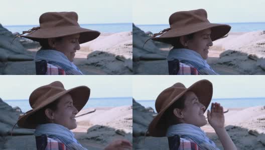 一个快乐的年轻女孩戴着帽子微笑着站在海滩上高清在线视频素材下载