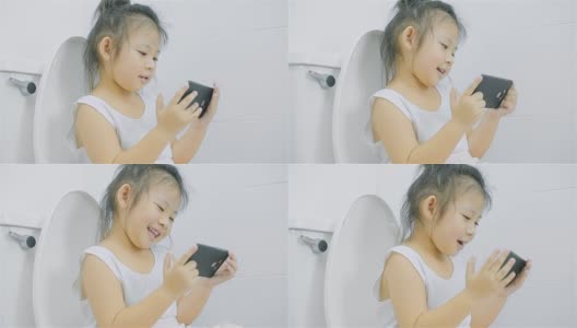 看智能手机的小女孩坐在厕所的马桶上高清在线视频素材下载