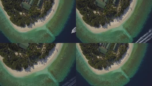 无人机镜头降落到空旷的热带白色沙滩上，只有一对夫妇躺在马尔代夫的环礁岛度假村的躺椅上晒太阳，那里有棕榈树的影子和蓝绿色的印度洋。快艇正驶过。假期的隐私高清在线视频素材下载