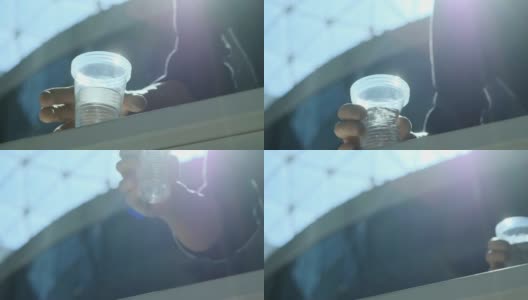 一个残疾人拿着一个塑料杯子喝水。一只义肢举起一杯水。独立完整的生活与假肢。底视图高清在线视频素材下载
