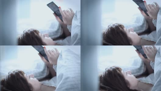 漂亮的黑发女人早上把头放在枕头上，在床上用电话，读一些信息，读新闻高清在线视频素材下载