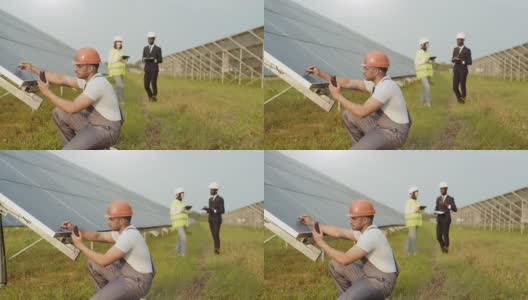 能源技术员戴着头盔，穿着制服，在户外用万用表测量太阳能电池板的电压。一群工程师用平板电脑和剪贴板站在背景上。靠近太阳能电池板的男子高清在线视频素材下载