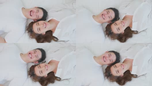 亚洲新婚夫妇躺在床上看着相机的肖像。漂亮漂亮的年轻男女穿着睡衣在家里的卧室里享受清晨的活动。家庭关系的概念高清在线视频素材下载