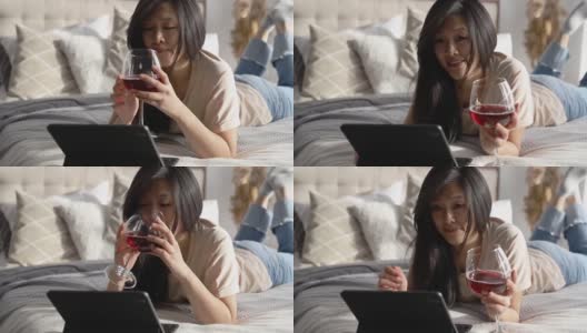 快乐美丽的女人在休闲的衣服上讲视频电话数字平板电脑躺在床上。玩游戏，网上购物放松。高清在线视频素材下载