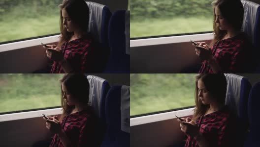严肃，放松的年轻女孩坐在火车靠窗的地方。乘现代火车旅行。长头发的女孩正在用她的手机滚动或打字。红色格子衬衫。侧视图高清在线视频素材下载