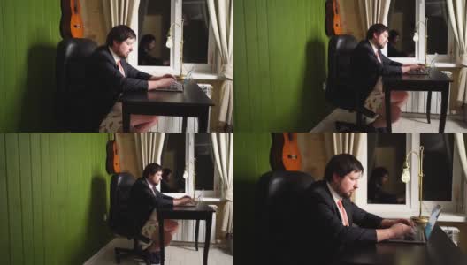 一个穿裤子、夹克、领带的男人晚上在家庭办公室的电脑前工作高清在线视频素材下载