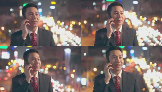 亚洲年轻商人站在户外使用手机在城市的市中心晚上。他在用智能手机聊天，笑得很开心。这位商人对现代网络技术很满意。高清在线视频素材下载