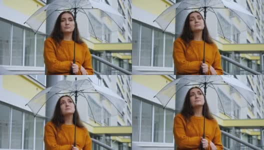 悲伤的女人在雨中站在透明的伞下，背景是一幢公寓高清在线视频素材下载