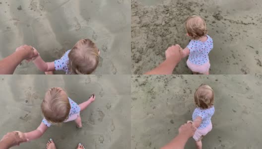 蹒跚学步的小女孩在海滩上牵着妈妈的手，从山顶往下看高清在线视频素材下载