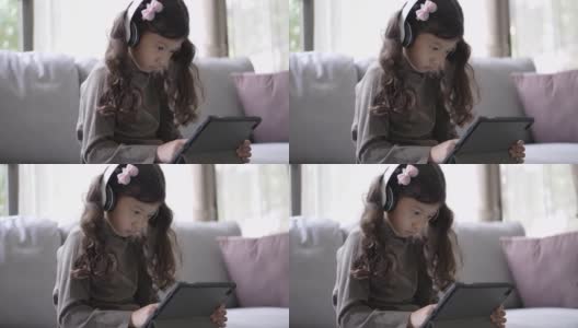 小女孩在家里的客厅里用数码平板电脑在线学习高清在线视频素材下载