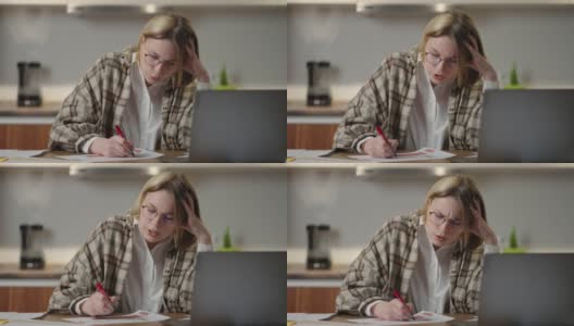 这位女士在家远程工作，坐在桌子旁，用笔记本电脑和毡尖笔在图表上标记数据。紧张地在视频上说话高清在线视频素材下载
