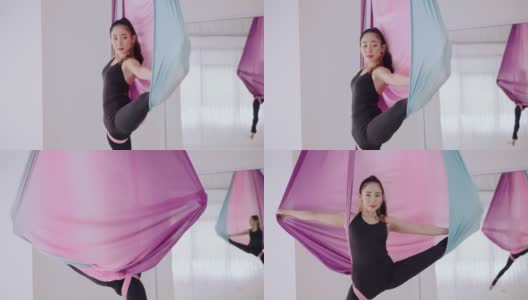 调整形状的时间。健康年轻的亚洲妇女在黑色运动服做瑜伽飞行与晾衣绳姿势空中使用彩色吊床。空中反重力瑜伽女子用彩色丝带表演瑜伽飞行。灵活性和浓度。高清在线视频素材下载