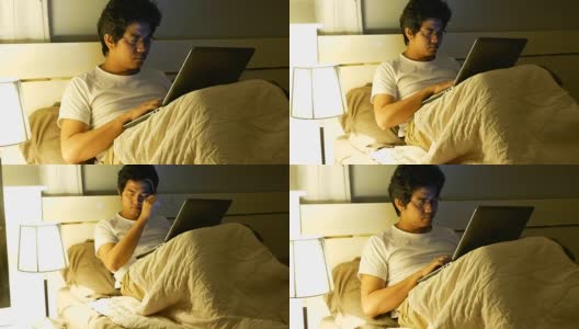 亚洲人电脑程序员工作到很晚，在卧室里使用笔记本电脑高清在线视频素材下载