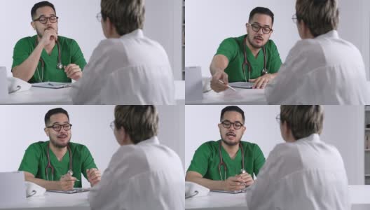 身着外科制服的年轻亚洲男医生微笑着向在检查室使用笔记本电脑的女病人讲解。高清在线视频素材下载