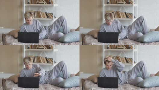 早晨，穿着睡衣的一名男子坐在床上，一边看着笔记本电脑屏幕一边聊天高清在线视频素材下载