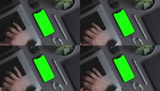 一个绿色屏幕的手机放在他的桌面上，正在笔记本电脑上打字高清在线视频素材下载