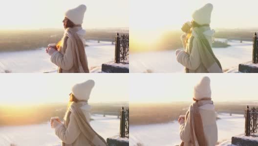 幸福微笑的年轻女子站在观景台上看日落，手里拿着一杯热咖啡。高清在线视频素材下载